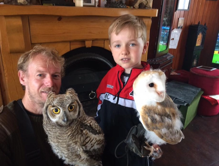 A man and a young boy standing together indoors while each holds a perched owl.