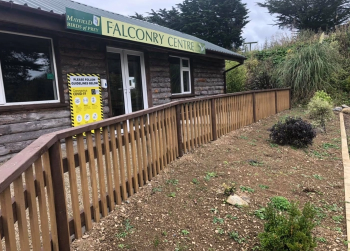 Exterior of the Mayfield Birds of Prey Falconry Centre, featuring a wooden building with a COVID-19 safety sign.