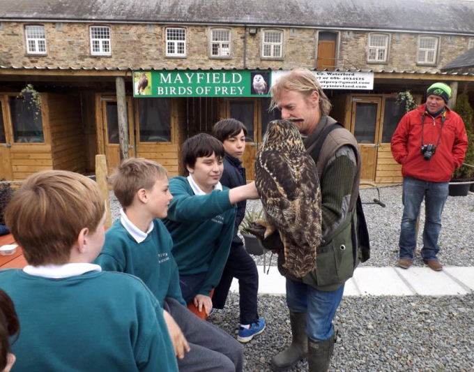 A group of students in green uniforms learning about a large owl held by a handler at Mayfield Birds of Prey.