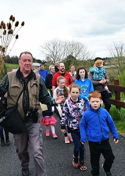 A guide leading a group of adults and children on an educational nature walk outdoors.