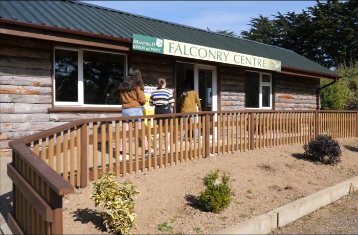 Visitors entering the Mayfield Birds of Prey Falconry Centre wooden log cabin building.