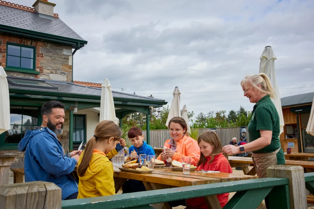 A family sitting at an outdoor restaurant table being served food by a smiling waitress.