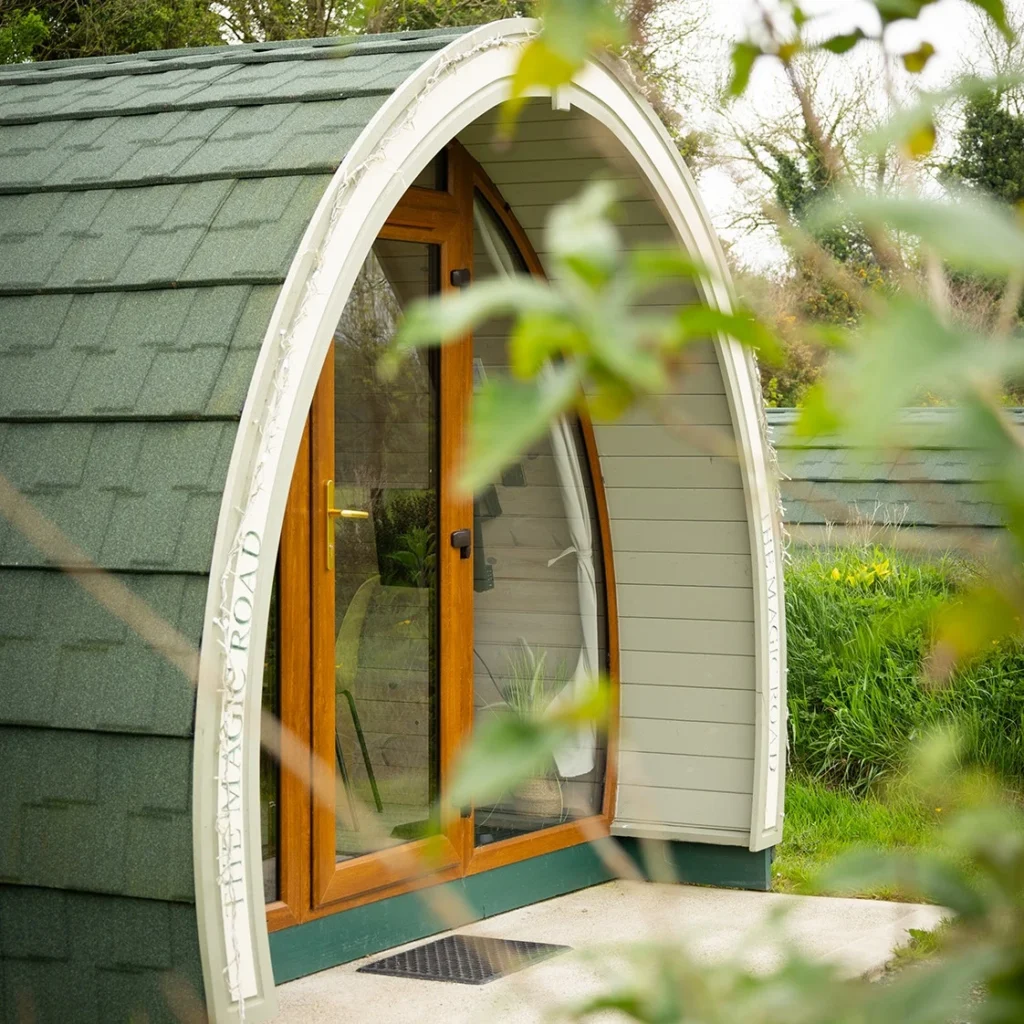 A green, arched wooden glamping pod with glass doors.
