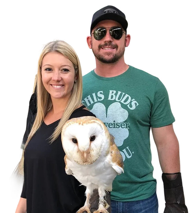 A smiling man and woman pose with a white Barn Owl perched on a gloved hand.
