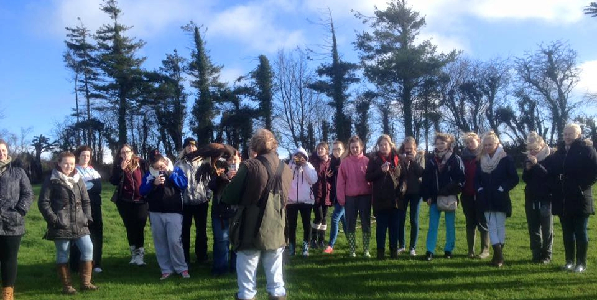 A large group of people gathers in a grassy field to watch a falconry demonstration with a hawk.