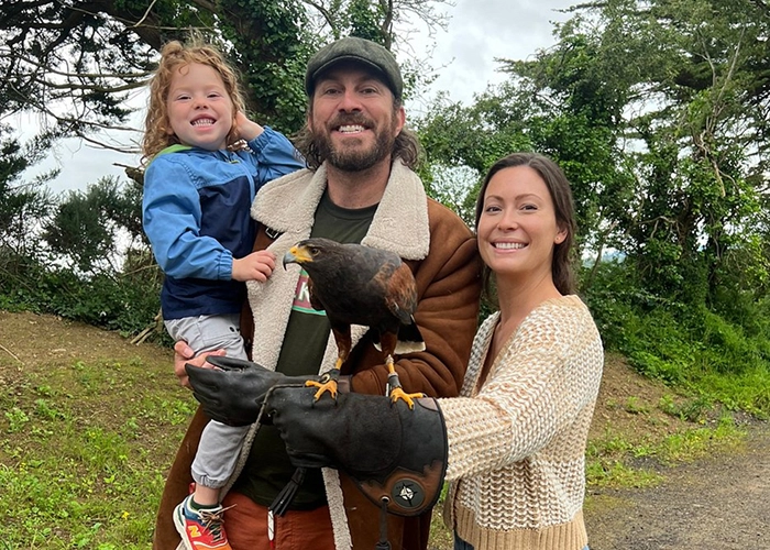 A smiling family poses outdoors with a hawk perched on a leather glove.