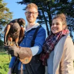 A young couple holding a hawk, smiling.